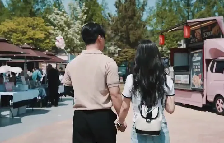 야외 행사장에서 손을 잡고 걷는 남녀의 뒷모습